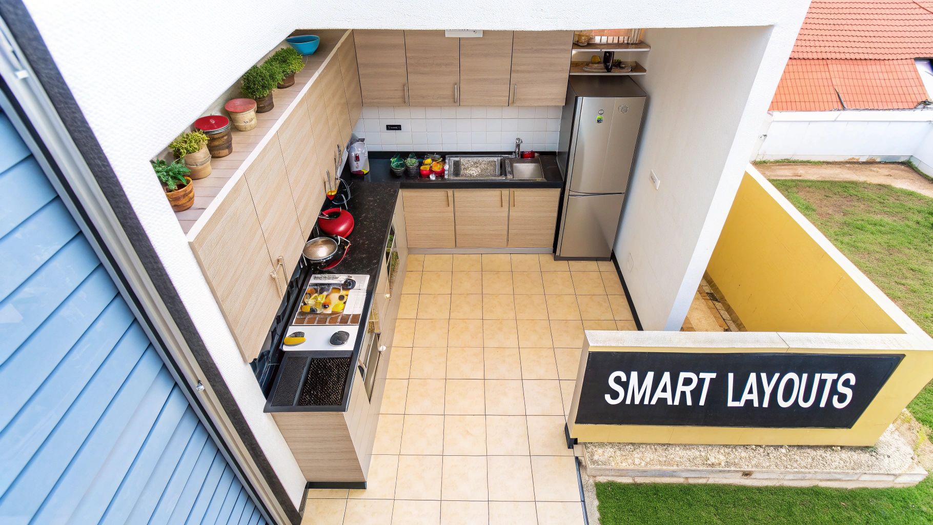 Overhead view of a modern outdoor kitchen featuring light wood cabinets, black countertops, stainless steel appliances, and potted plants.