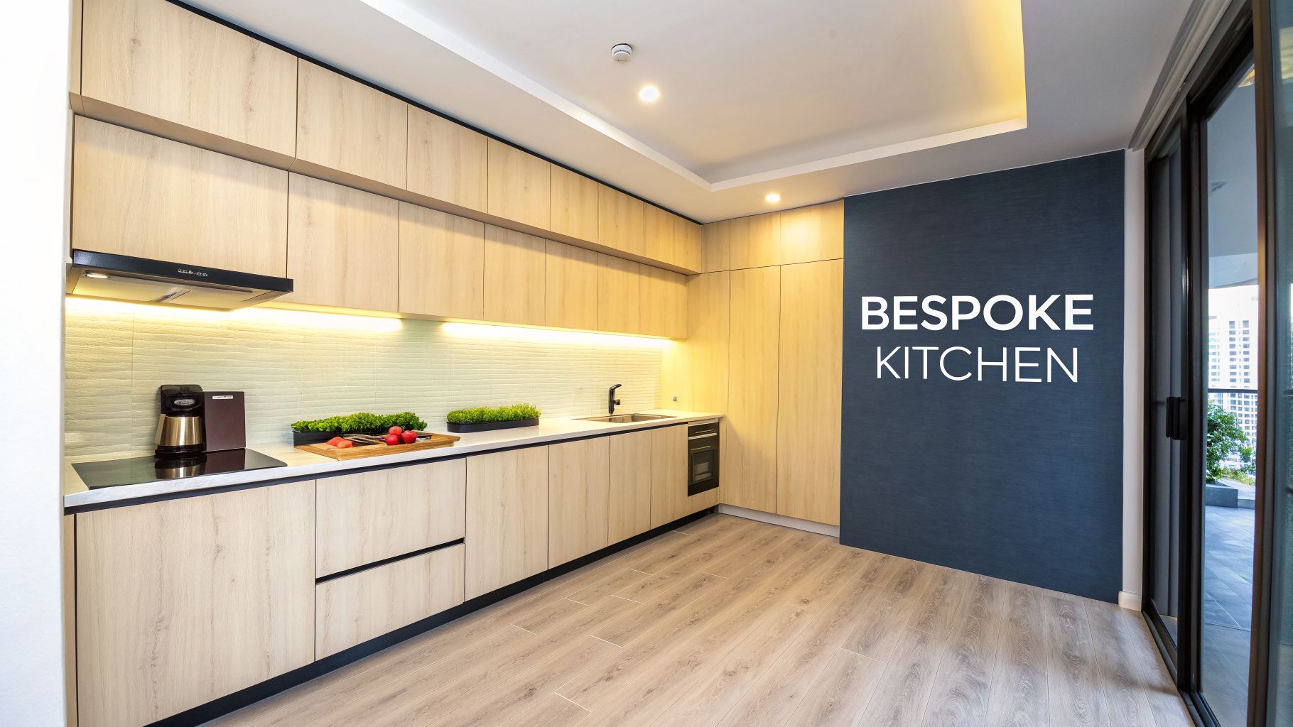 A modern bespoke kitchen featuring light wood cabinets, a dark blue accent wall, and cooking appliances.